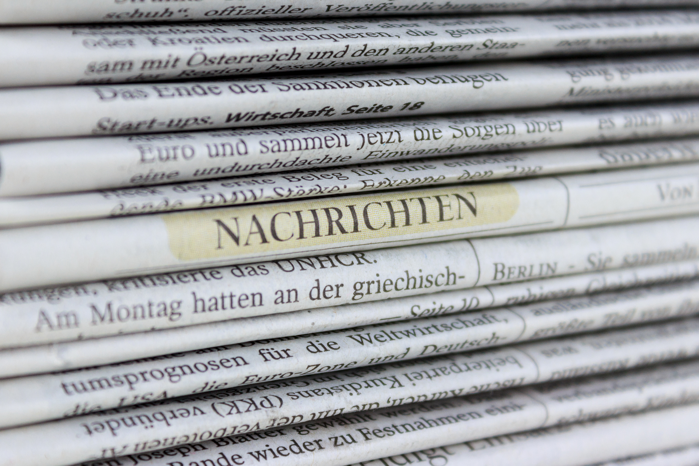 Ein Stapel an Zeitungen. Bei einer der Zeitungen ist das Wort "Nachrichten" farblich hervogehoben worden.